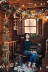 Fototapeta na wymiar young caucasian beautiful girl sits in the cozy yard of a village house decorated for the New Year