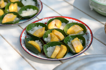 Thai famous dessert, Khaoniao Mamuang, Mango Sticky Rice topped with a coconut milk placed on banana leaves cups arranged in a circle in round enameled tray.