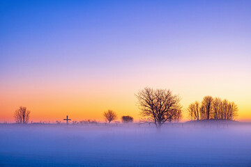 Fototapeta na wymiar Winter sunrise with fog and a religious cross in silhouette