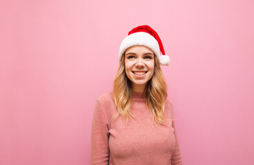 Portrait of happy girl in a santa hat on a pink background, looking away and smiling. Christmas lady in cute happy clothes isolated on pink background. Copy space