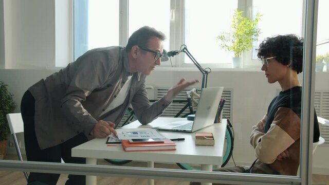 Evil mature businessman is shouting at stressed young woman gesturing expressing negative emotions in office. Business and corporate relationship concept.