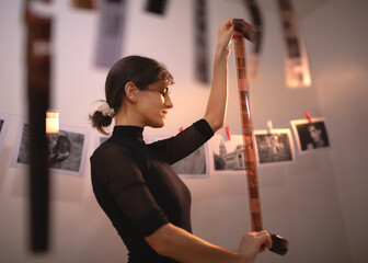 Young creative female holding filmstrip. Portrait of creative girl photographer in photo studio darkroom. Developing analog camera film