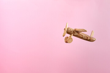 Handmade wooden airplane toy flying on a pastel pink background.