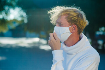 A young man in a medical protective mask, anxiously looking to the side, adjusting the mask.