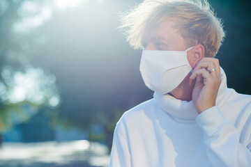 A young man in a medical protective mask, anxiously looking to the side, adjusting the mask.