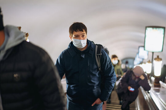 caucasian man wearing medicine mask standing on the up escalator of underground station in saint petersburg, Russia. Image with selective focus