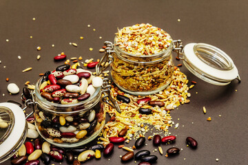 Mix of variety of cereals and beans in glass jars on black stone background