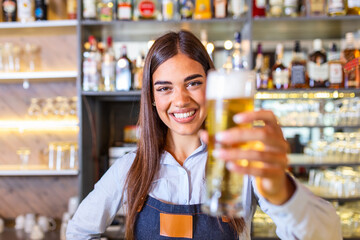Young woman serving draft beer. Smiling female bartender pouring from tap fresh beer into the glass in pub.