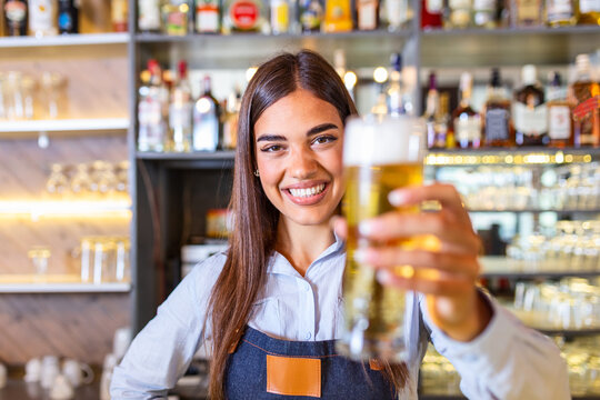 Young woman serving draft beer. Smiling female bartender pouring from tap fresh beer into the glass in pub.