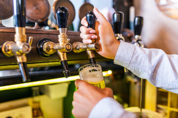Hand of bartender pouring a large lager beer in tap. Bright and modern neon light, females hands. Pouring beer for client.