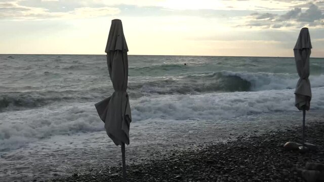 Storm at the sea coast. Closed beach umbrella, strong wind, big waves with lot of foam. Summer evening, bright dky and gray water.