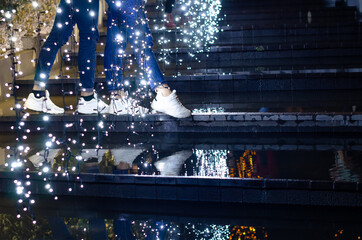 Christmas holiday in the city park. Feet of girls on the steps against the background of blue glowing Christmas garlands. Weekend concept. Details, people
