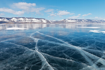 Frozen Baikal Lake on a sunny February day. Beautiful blue smooth ice with cracks in the Small Sea Strait. Poles mark the ice road to Olkhon Island. Winter ice travel. Natural background