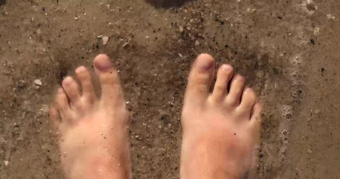 4k Female bare feet on the sand on a sunny day. Girl leg walking on the sand of the beach with the sea water. Travel concept.