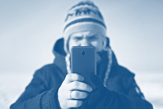 Middle-aged man in winter hat making selfie with smart phone, trendy toned photo