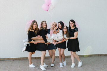Fototapeta premium Beautiful sexy young girls hold pink air balloons in dress and veil on bachelor party. Bride hugging bridesmaids smiling outdoors and celebrating bachelorette party. Maiden evening, Hen-parties.