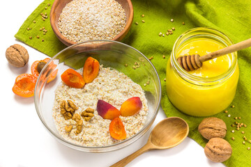 Buckwheat porridge in a glass dish with fresh apricots, walnuts and honey on tablecloth isolated on white background. Healthy food concept