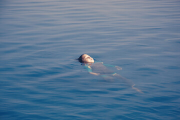 Joyful boy swimming with backstroke style on the infinity pool and sea view on the background