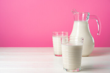 Glassware with fresh milk against pink pastel background