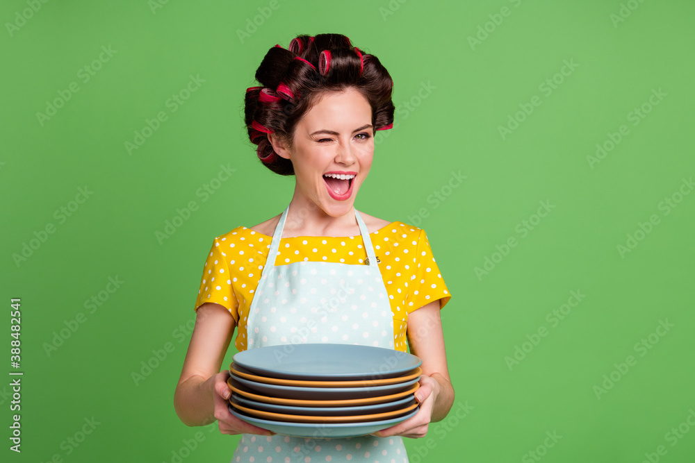 Sticker Portrait of her she nice attractive glamorous cheerful cheery glad flirty maid wearing curlers holding in hands pile stack plates winking fast service isolated over green color background