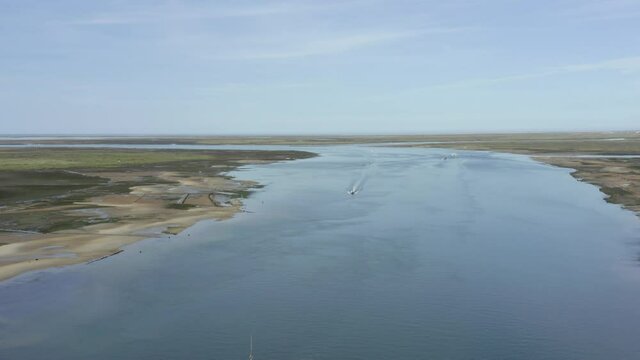 Boats sail though an oceanic inlet in olhao on a beautiful blue sky day, drone aerial
