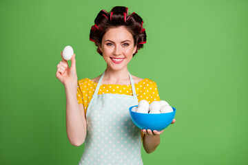 Photo of lovely adorable young girl roller hairstyle toothy smile hold bowl eggs presenting showing...