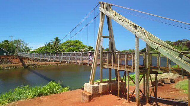 4K right to left panning motion of woman crossing the Hanapepe swinging bridge, Wooden bridge built in early 1900,Kauai,Hawaii,USA