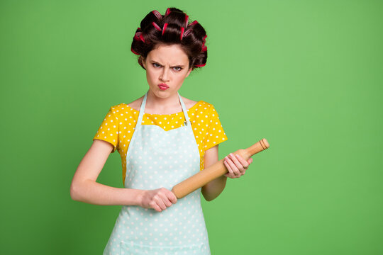 Photo of pretty angry young girl roller hairdo threatening look hold rolling pin ready punish husband called lunch not tasty wear dotted apron shirt isolated green color background