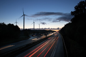 German Autobahn leading past wind turbines towards power plant at sunrise with light trails and...