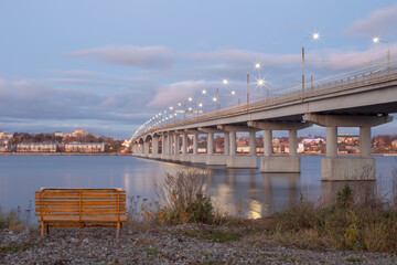 empty bench against the background of the bridge over the Volga river in Kostroma in the evening