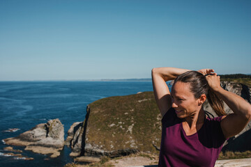 Athletic woman making herself a ponytail in the hair, with the coastline in the background