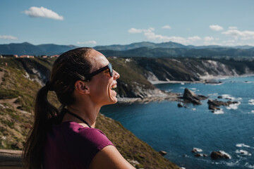 Fototapeta na wymiar White woman laughing while look at the ocean in a coastal cliff, in Asturias, Spain.