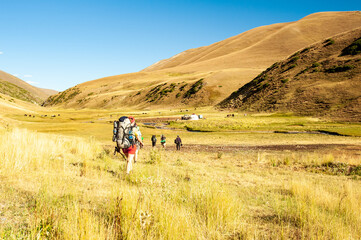 Obraz premium Group of trekkers descending rocky pass with mountain top views heading to yurt settlement. Young men and women hiking near Sary Chelek lake, Sary-Chelek Jalal Abad region, Kyrgyzstan, Trekking 