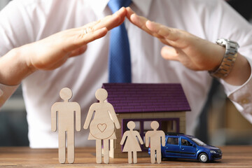 Man in tie holds his hands over wooden men with toy house and car closeup. Social guarantees for...