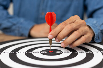 Fototapeta premium Hand Businessman holding arrow directed towards dart board target, successful business idea, A man wearing a jean shirt with a red dart Centered on the target