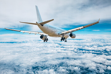 Commercial airplane flying above blue sky and white clouds.