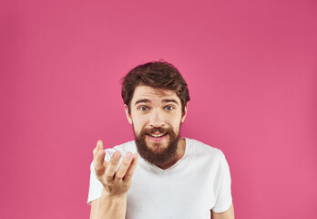 Happy young man on a pink background in a white T-shirt and a thick beard gesticulate with his hands