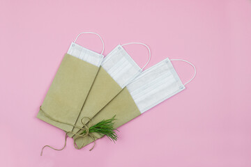 Medical protective masks in craft paper envelope. DIY bow with Christmas tree branch. Delicate pink background. Close up. Copy space