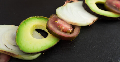 chopped vegetables black tomatoes, avocado and onions against black stone board