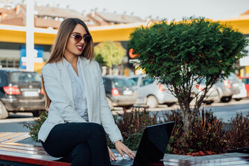 Beautiful businesswoman working on a laptop while sitting on a bench. 