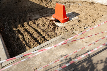 Dangerous open hatch without cover and a warning fence on the road