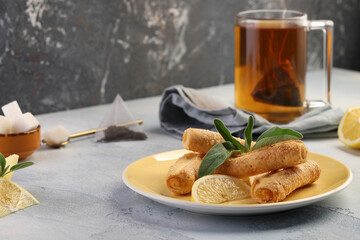 Lemon rolls of puff pastry with lemon jam, garnished with sage leaves on a yellow plate, and a mug of black tea. Delicious dessert.