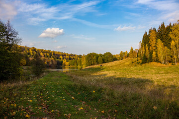 Green valley and blue sky on an autumn day. Colorful view of meadows and forest

