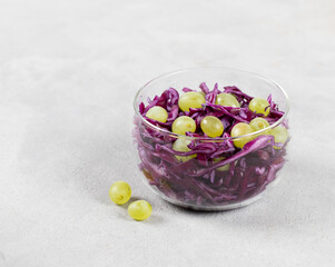 Vegetable berry salad of fresh red cabbage with green grapes in a glass bowl on a light background