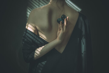 Back portrait of a woman with a v backless dress with the arm twisted back holding plums, beautiful scapula showing with shadows stripes reflections. Concept: abundance, autumn/fall harvest, artistry