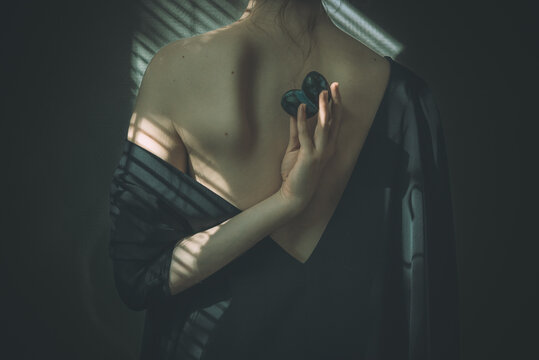 Back portrait of a woman with a v backless dress with the arm twisted back holding plums, beautiful scapula showing with shadows stripes reflections. Concept: abundance, autumn/fall harvest, artistry