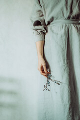 Mid section of a woman in an oversized grey organic linen holding a branch of winter berries in the hand. Concept: minimalism, simplicity, beauty, boho, cosy, comfy wear