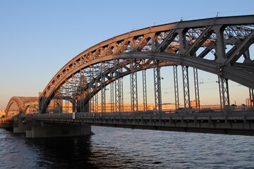 Three-span bridge with two arched trusses at sunset. (Peter the Great Bridge. Years of construction 1908-1911) 