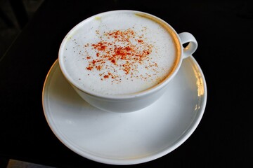 Close up of cup with cappuccino coffee served with cinnamon in black background.