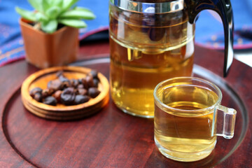 Cascara or coffee cherry tea in glass with dried cherry coffee and tea pot on wooden plate background. Concept for health and eco-friendly unique beverage.